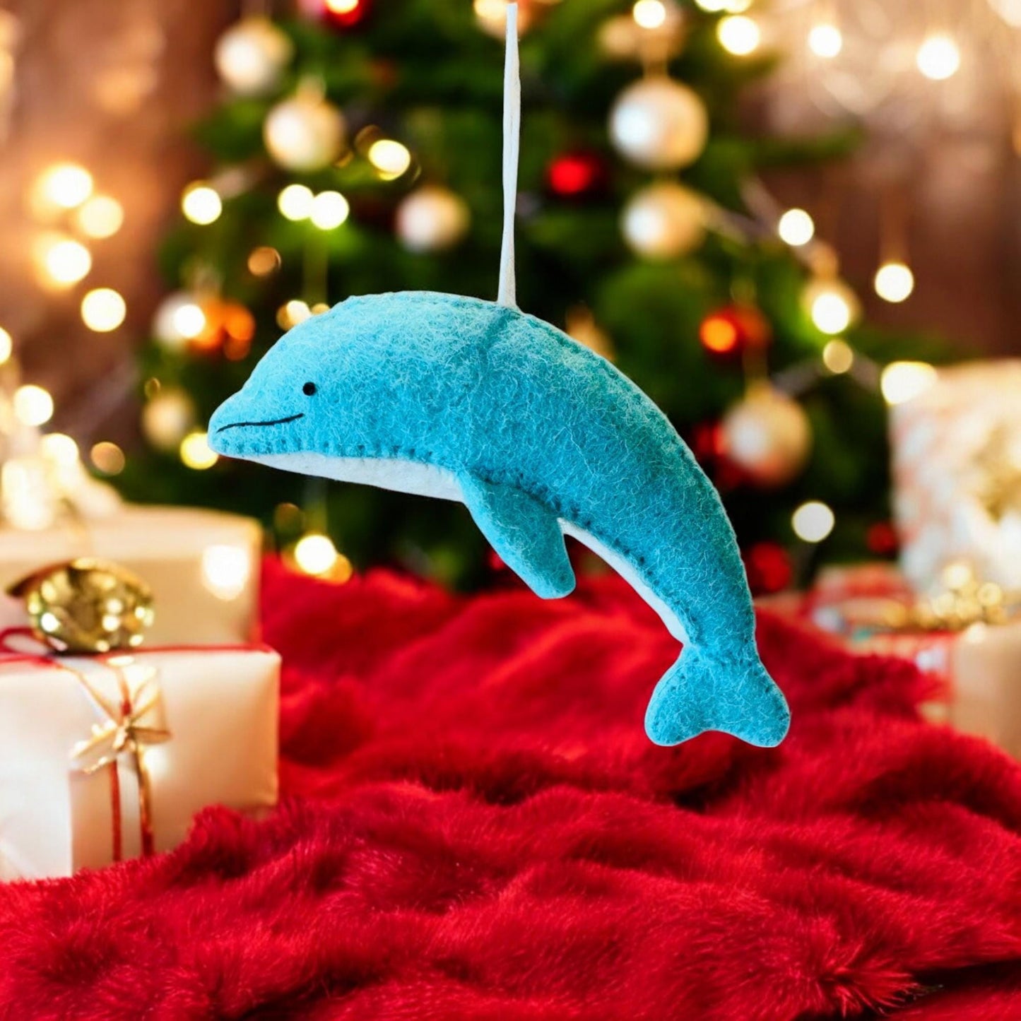 Blue dolphin ornament on a red surface with a Christmas tree in the background