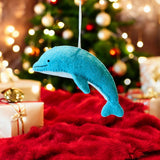 Blue dolphin ornament on a red surface with a Christmas tree in the background