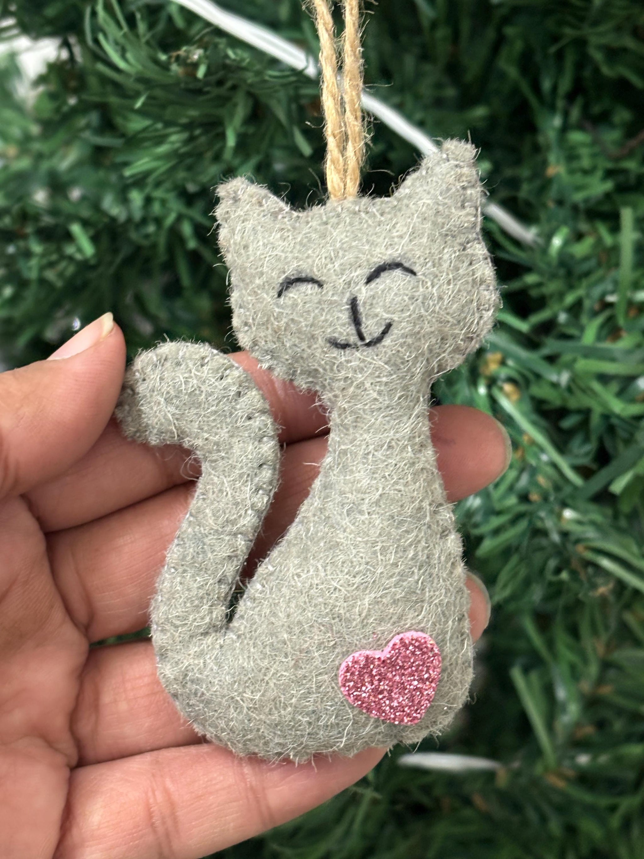 Small gray cat ornament with a pink heart on a hand against a green background