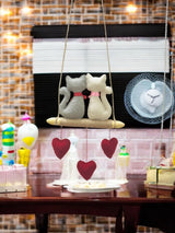 Decorative setup with cat-shaped objects on a swing against a textured wall.