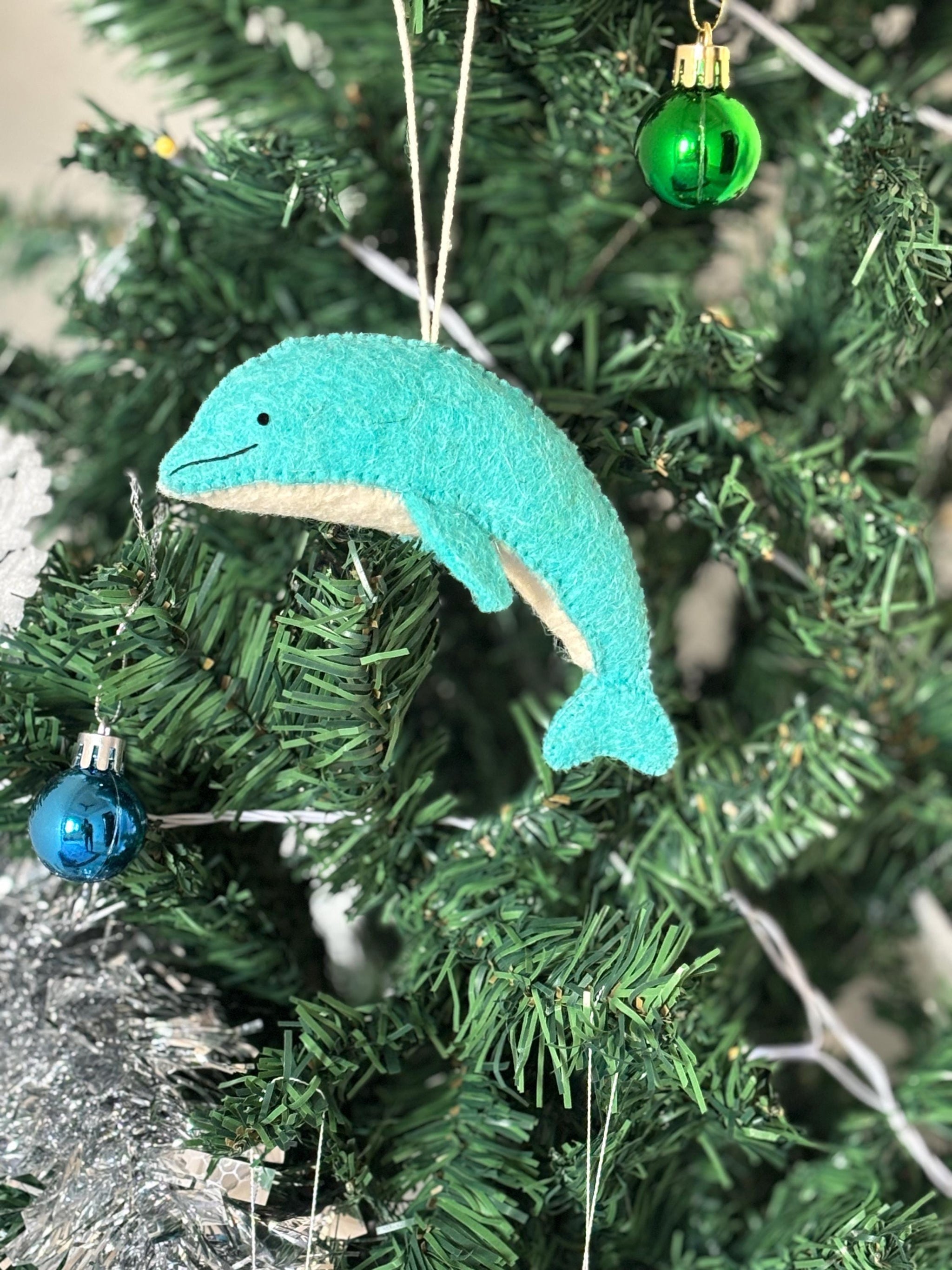 Teal dolphin ornament hanging on a Christmas tree with other decorations.