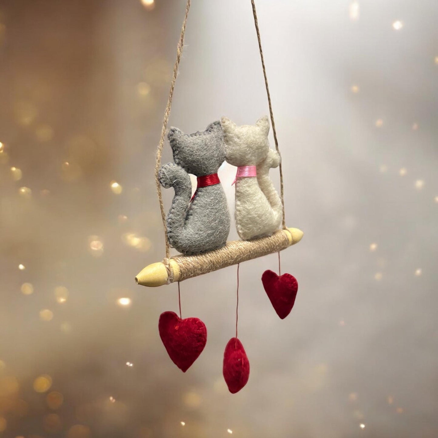 Two plush cats on a swing with heart decorations against a soft, blurred background