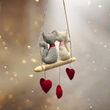 Two plush cats on a swing with heart decorations against a soft, blurred background