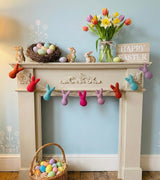 Decorative Easter mantel with colorful eggs, tulips, and bunny decorations on a fireplace.