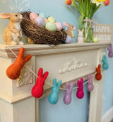 Decorative Easter mantel with colorful bunny garland, nest of eggs, and rabbit figurine.