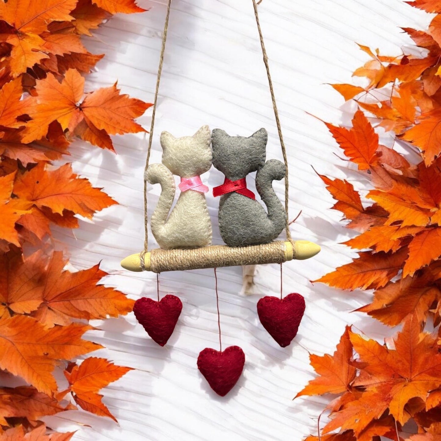 Two toy cats on a swing with autumn leaves around