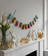 Easter-themed decor with bunny figurines, colorful eggs, and a felt carrot garland on a mantelpiece.