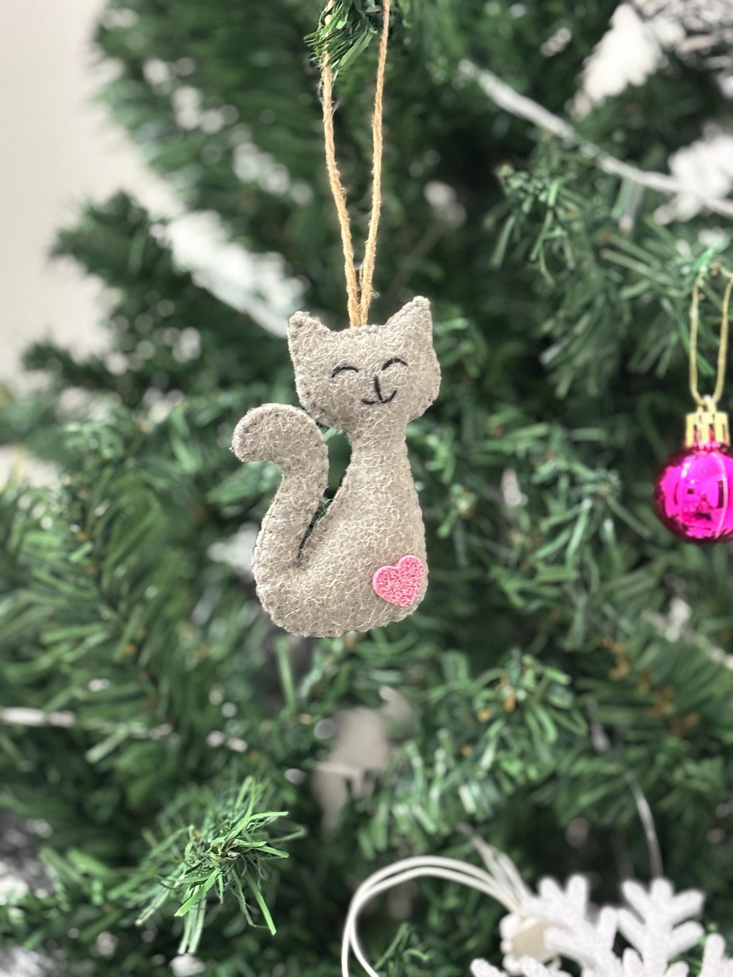 Cat-shaped ornament with a pink heart on a Christmas tree