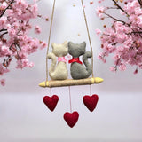 Two stuffed cats on a swing with pink cherry blossoms in the background