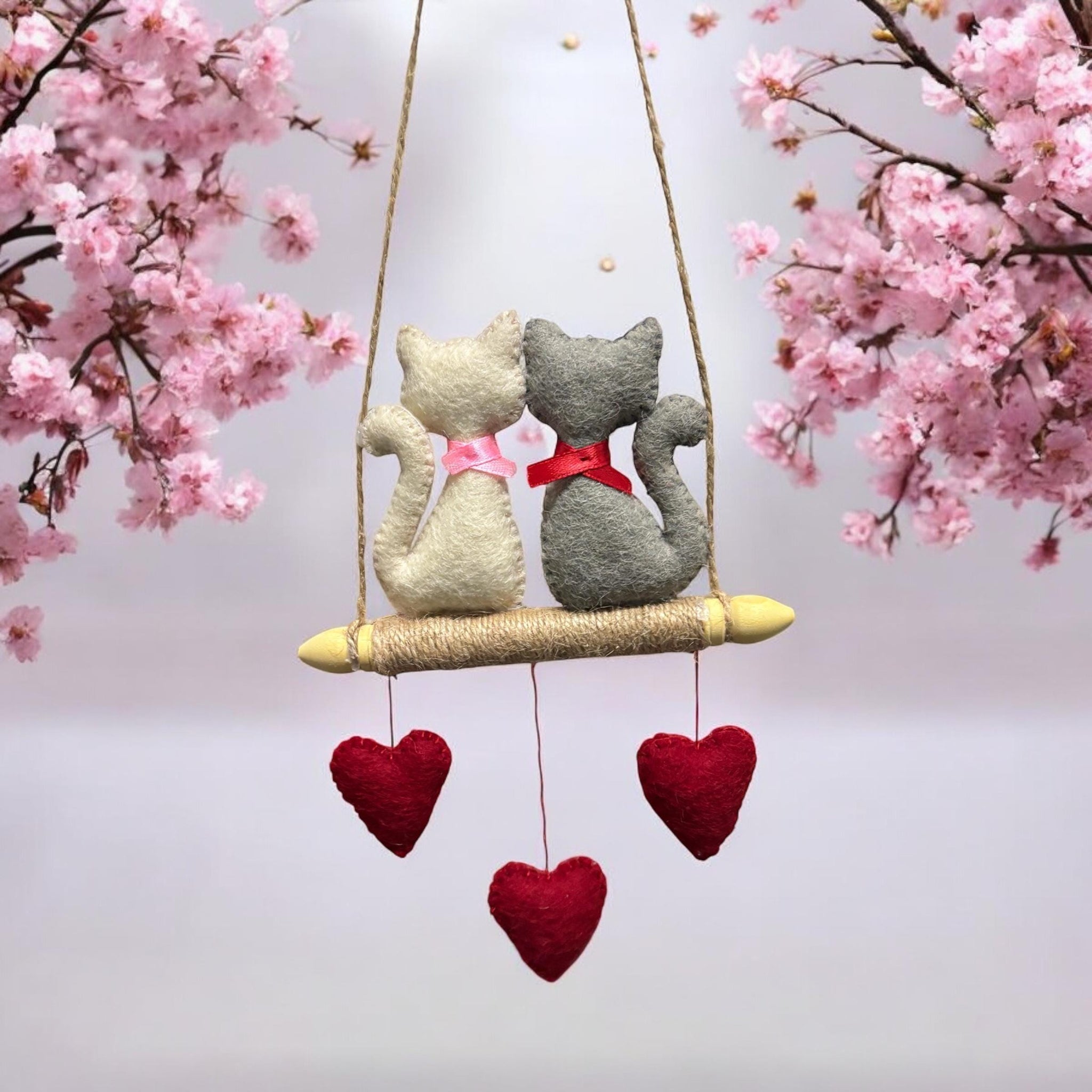 Two stuffed cats on a swing with pink cherry blossoms in the background