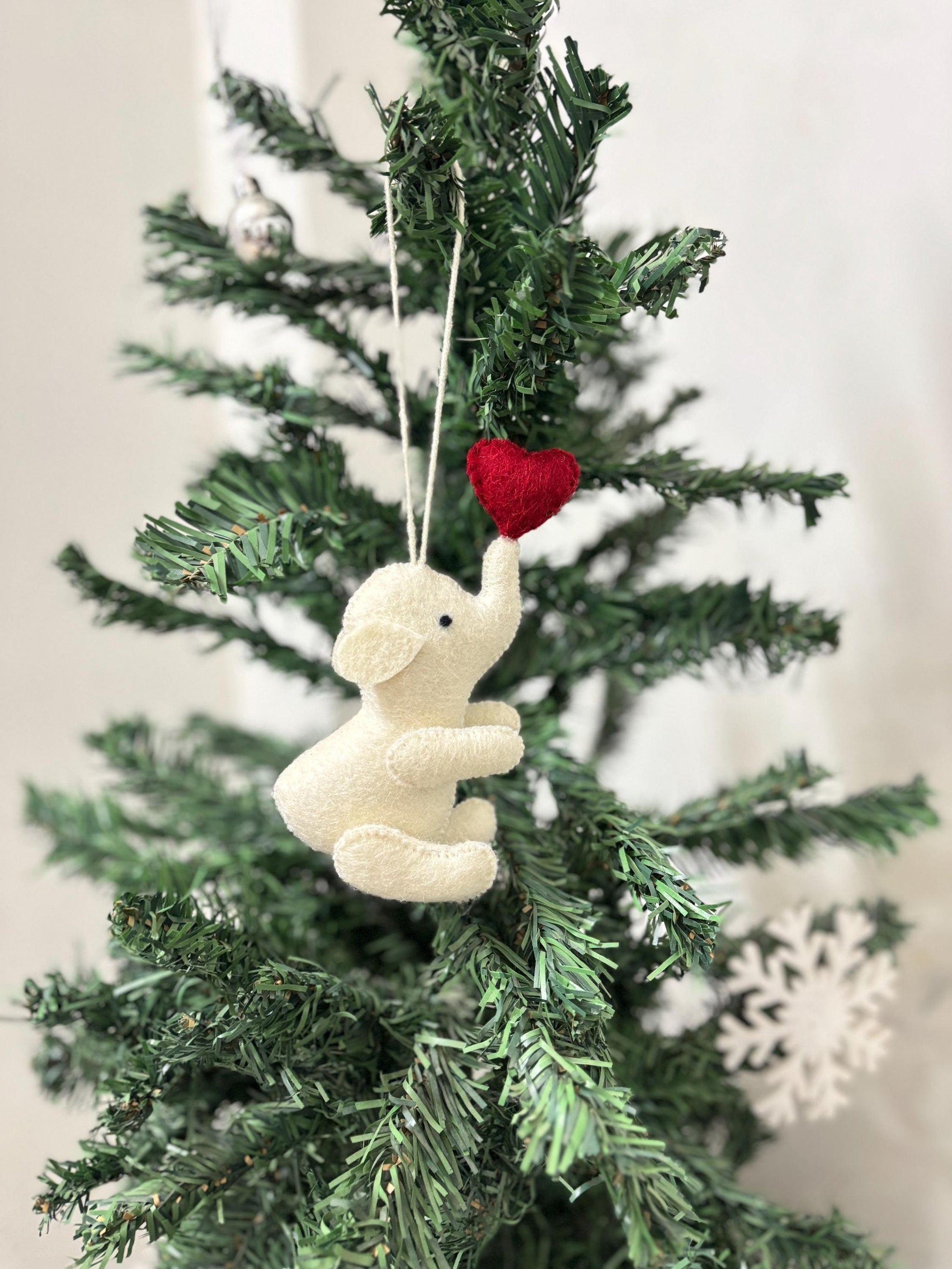 Decorative elephant ornament with a red heart hanging on a Christmas tree.