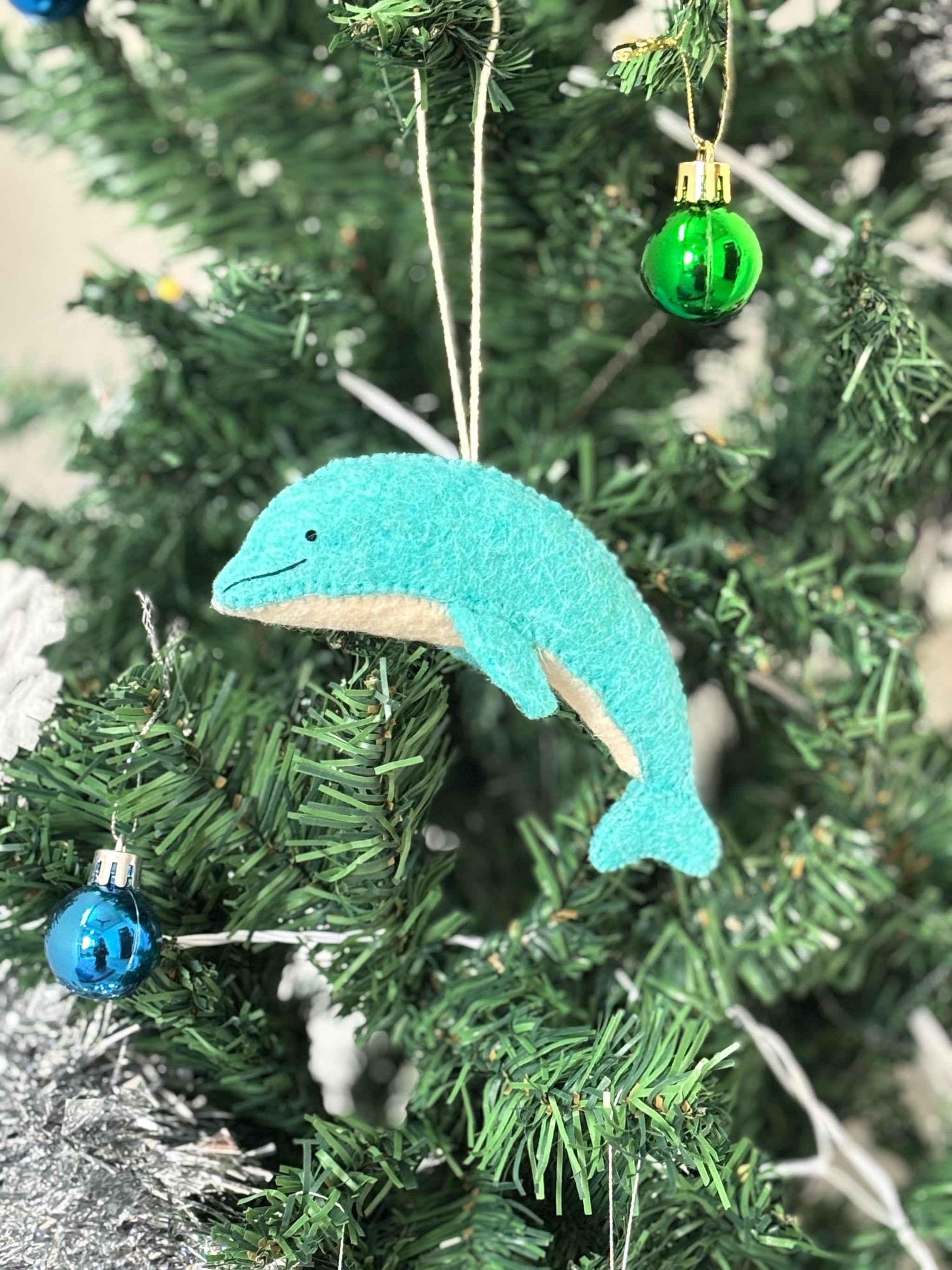 Teal dolphin ornament hanging on a Christmas tree with green and blue glass balls.