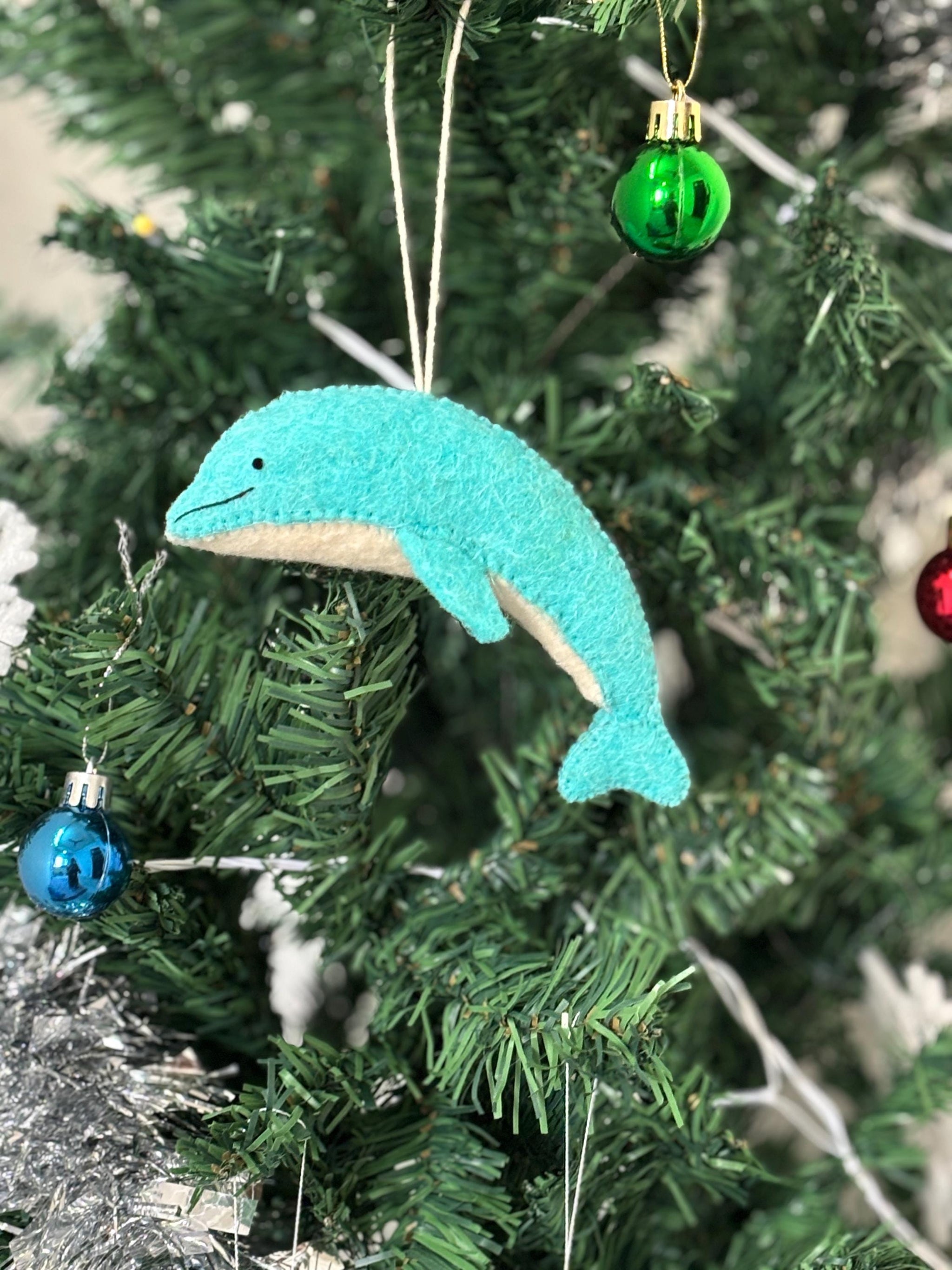 Blue dolphin ornament hanging on a Christmas tree with other decorations.