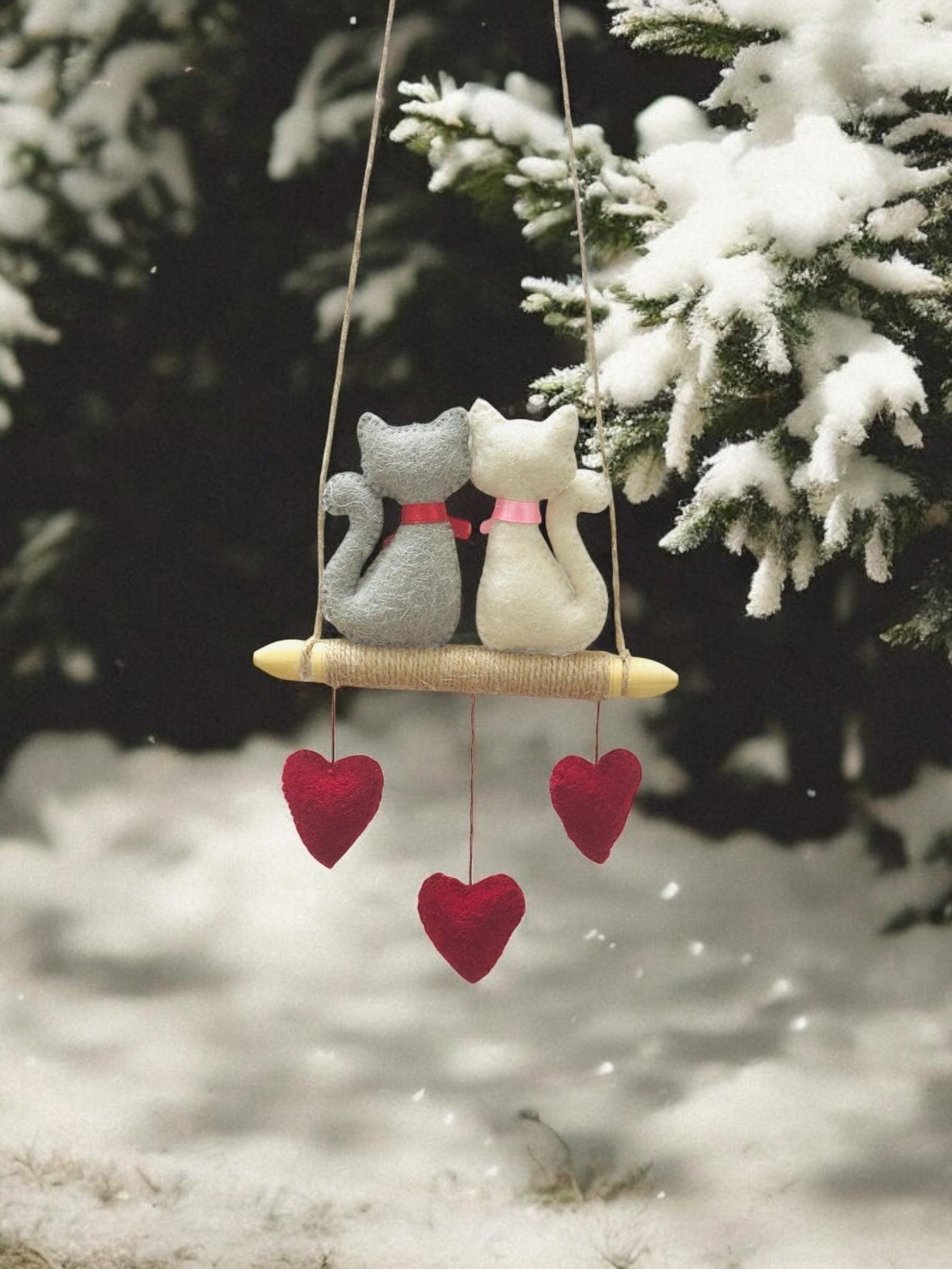 Decorative hanging cat ornament with red hearts against a snowy background