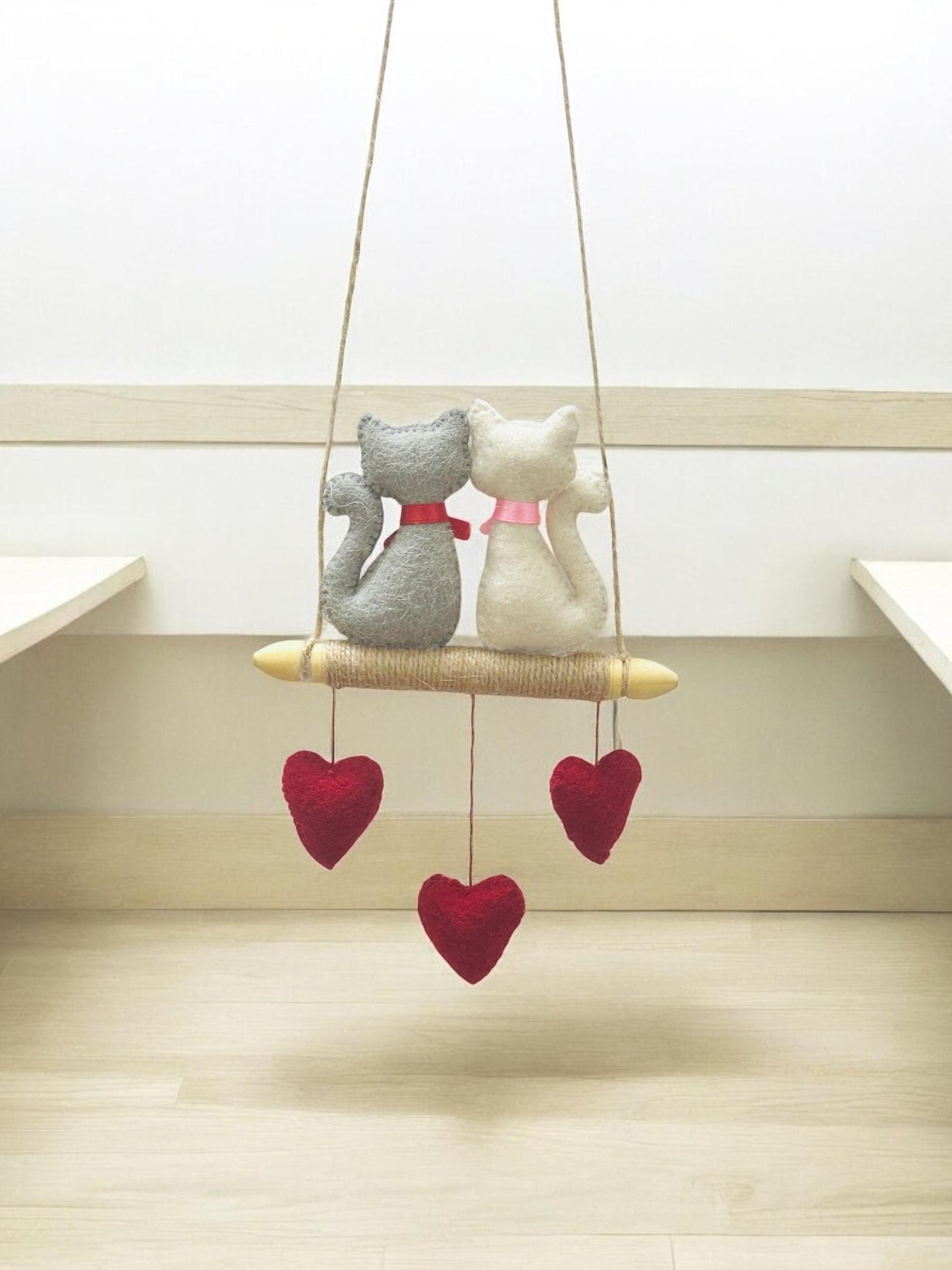 Decorative hanging with two cat-shaped figures and red heart shapes on a light wooden floor.