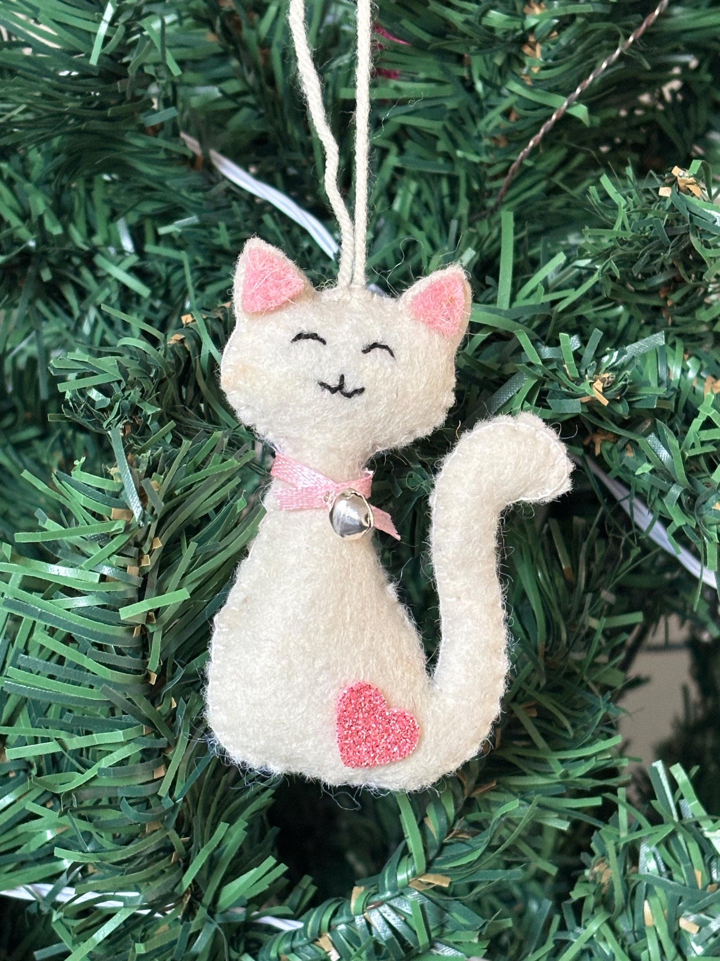 Cat-shaped ornament with pink accents hanging on a Christmas tree.