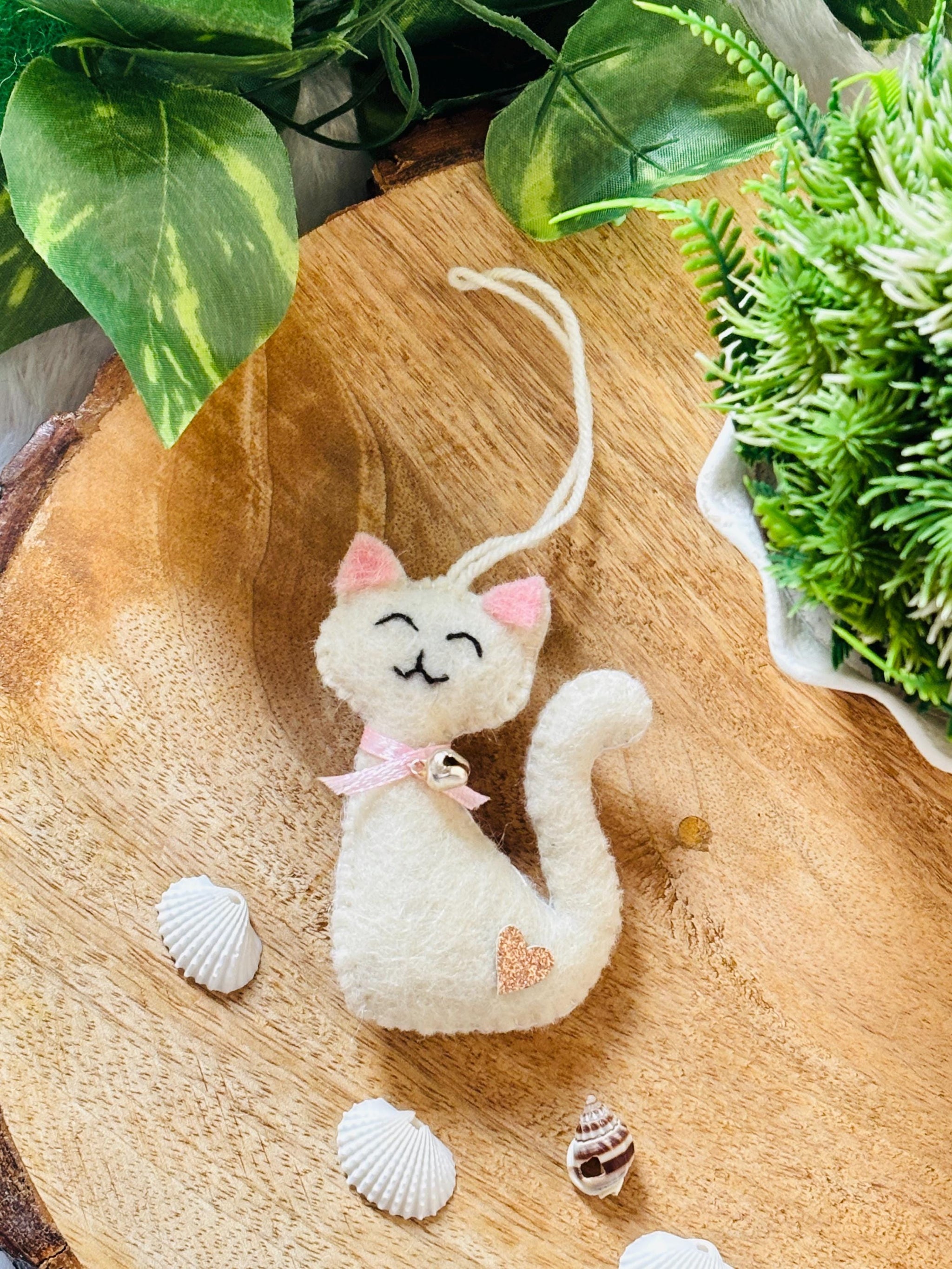 White cat plush toy with pink bow on a wooden surface with shells and plants.