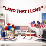 Decorated office desk with 'Land That I Love' banner, American flags, and 'God Bless America' sign.