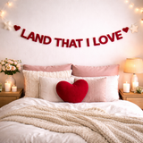 Decorative bedroom with 'LAND THAT I LOVE' banner, heart-shaped pillow, and candles.