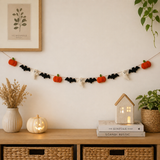Halloween-themed decorative string with pumpkins, bats, and ghosts on a wall above a wooden shelf with decor items.