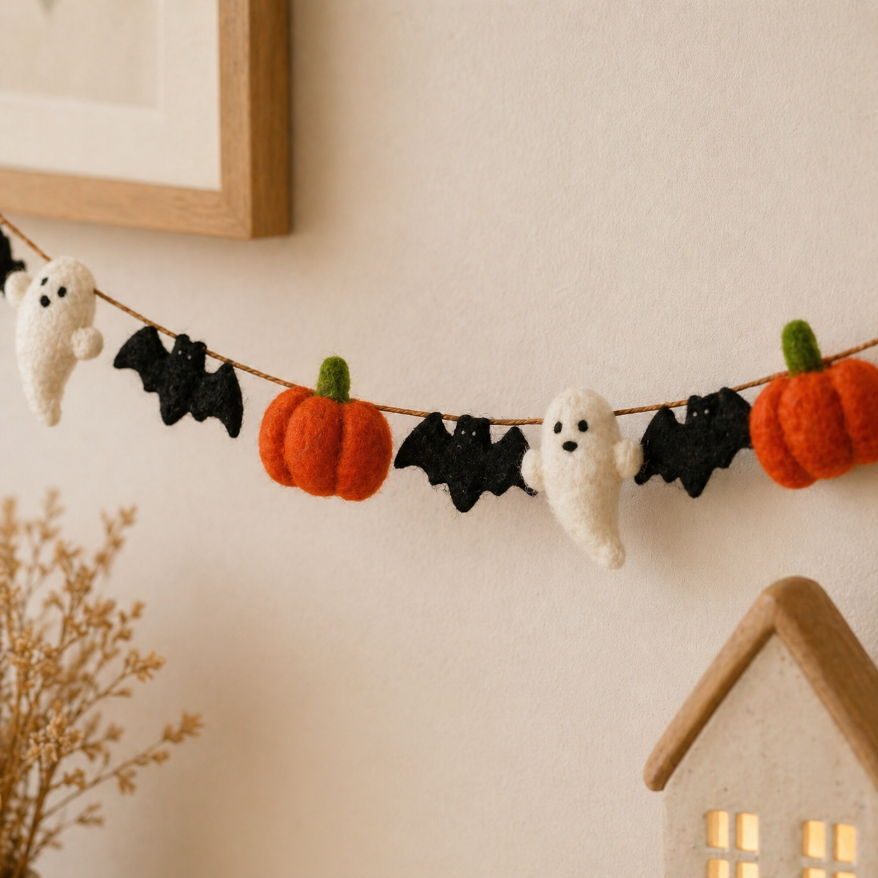 Halloween-themed decorative garland with pumpkins, ghosts, and bats on a wall.