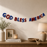 Decorative banner with 'GOD BLESS AMERICA' on a wall above a wooden shelf with decor items.