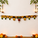 Decorative garland with flowers and swastikas on a white wall with candles and marigold flowers.