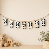 Decorative banner with panda plush toys hanging on a string against a beige wall.