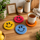 Colorful smiley face coasters on a wooden surface with a mug of tea.