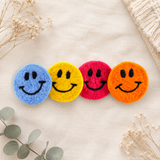 Four colorful smiley face coasters on a light surface with decorative elements.