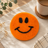 Orange smiley face coaster on a table with a cup of coffee and decorative elements.