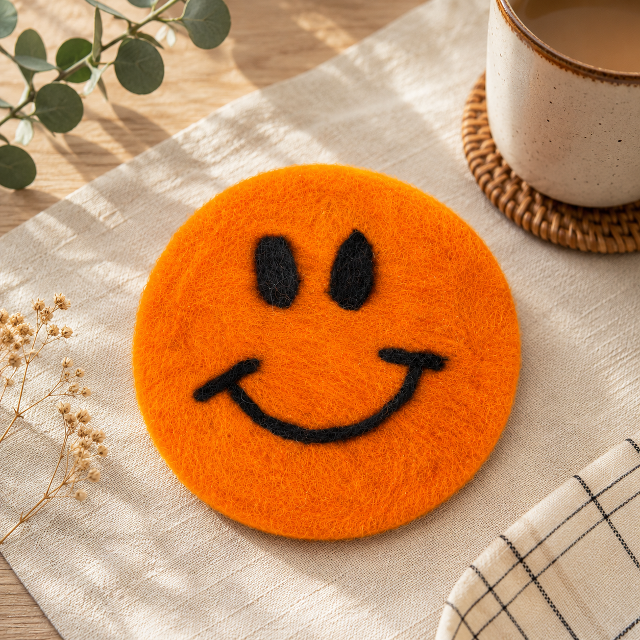 Orange smiley face coaster on a table with a cup of coffee and decorative elements.