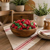 Wooden bowl filled with red and white decorative apples on a wooden table with a striped cloth.