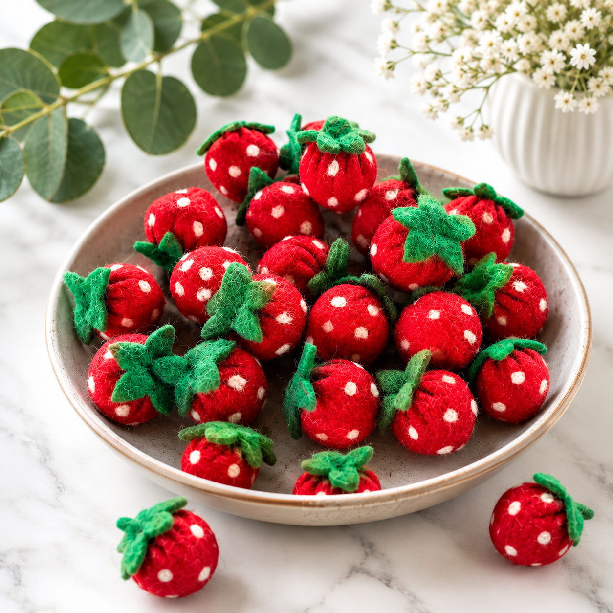 Felt strawberries with white polka dots on a marble surface with greenery.