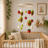 Nursery room with wooden crib, teddy bear, and decorative mobile with acorns and strawberries.