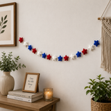 Decorative string of red, white, and blue stars on a wall above a wooden shelf with books and a plant.