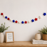 Decorative star garland on a wall above a wooden shelf with plants and a framed sign.