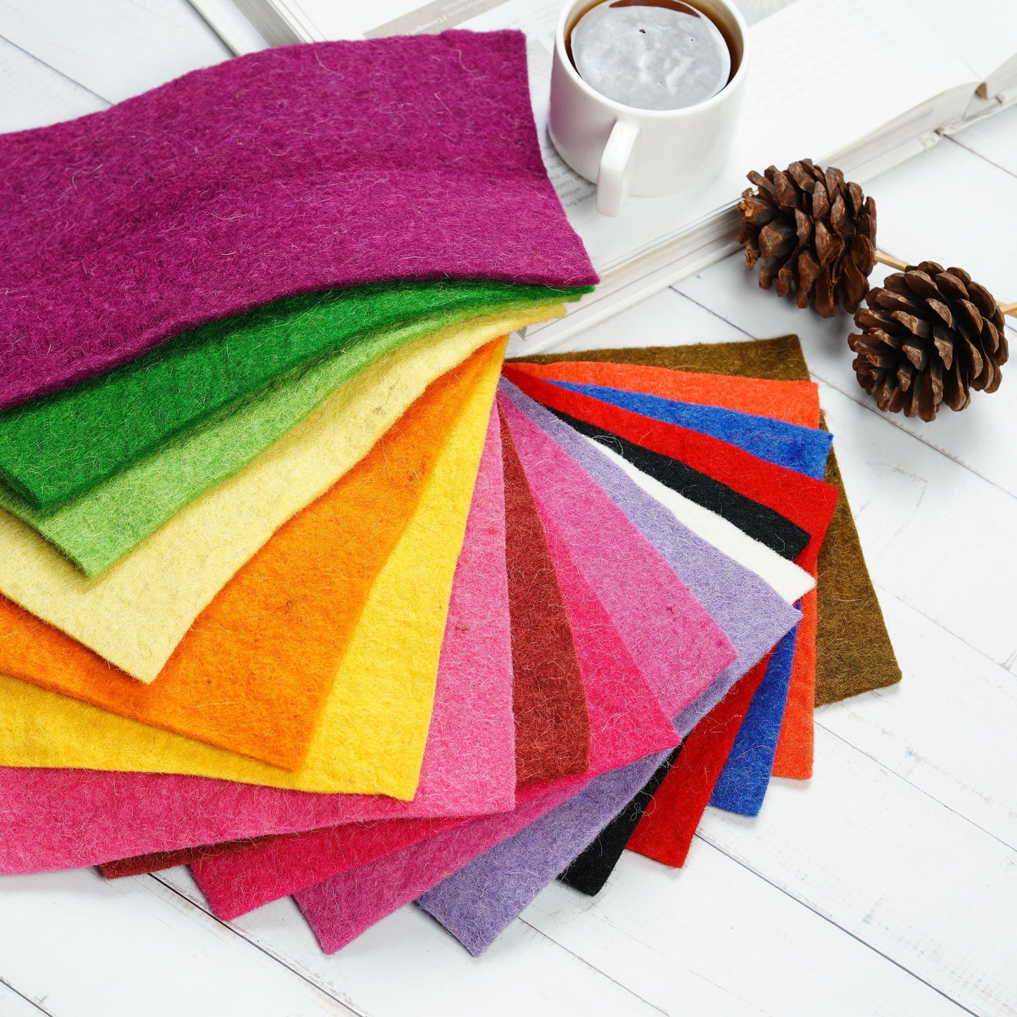 Colorful felt sheets arranged on a white surface with a cup of coffee and pine cones.