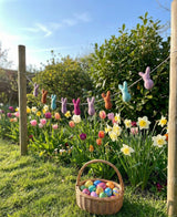 Decorative bunnies on a clothesline with a basket of Easter eggs in a garden setting.