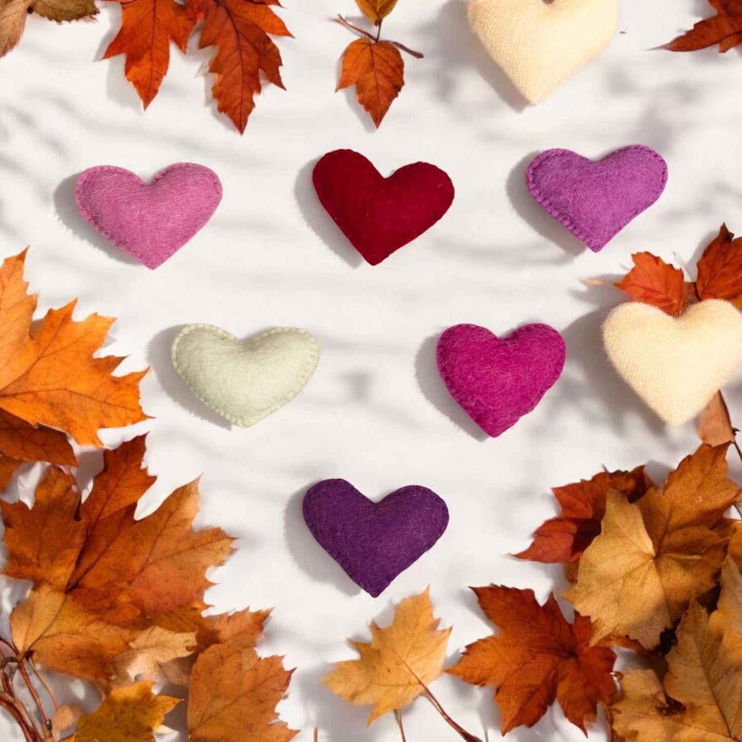 Colorful heart-shaped pillows on a white background with autumn leaves.