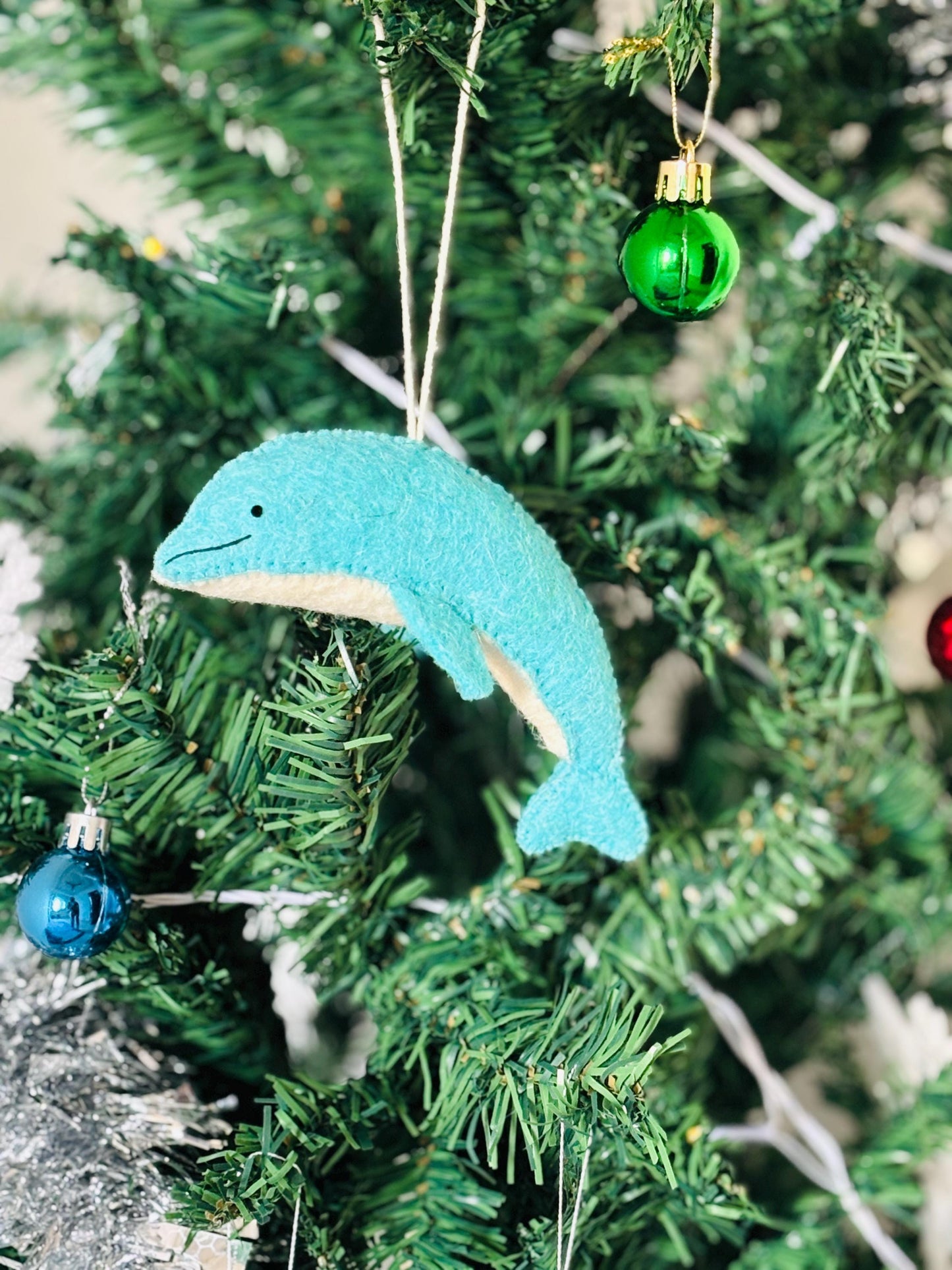 Blue dolphin ornament hanging on a Christmas tree with other decorations.