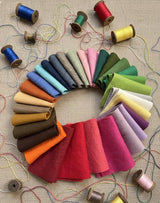Wool fabric swatches arranged in a circular pattern with spools of thread on a textured fabric background.