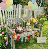 Decorative outdoor setup with Easter-themed items on a bench, including balloons and flowers, with 'Happy Easter' sign.