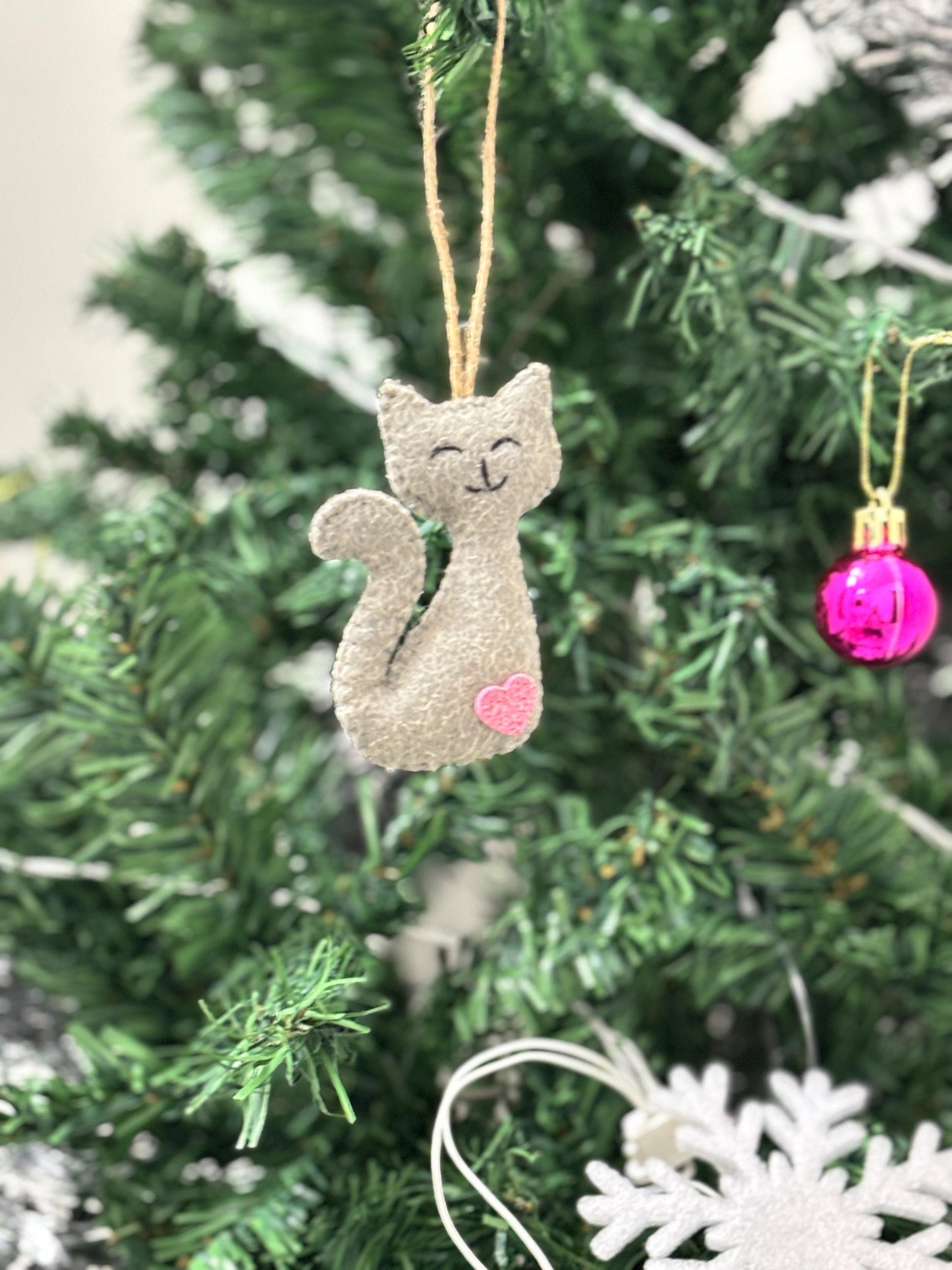 Cat-shaped ornament hanging on a Christmas tree with a pink heart.